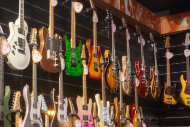 Krakow, Polonya - 30 Kasım 2025: Canlı renklere ve farklı tasarımlara sahip çeşitli elektro ve bas gitarları modern bir müzik mağazası ortamında sergilenmek üzere güzelce asıldı