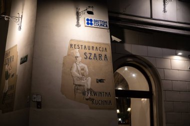 Krakow, Polonya - 30 Kasım 2025: Sienna caddesinin köşesinde İngiliz Konseyi, Restoran Szara ve Bar Szara tabelalarının sergilendiği eski bir binanın gece görüntüsü