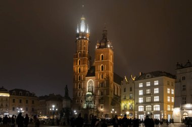 Krakow, Polonya - 30 Kasım 2025: St. Mary Bazilikası gece aydınlandı, etkileyici gotik ikiz kuleleri, karmaşık tuğla işleri ve hareketli tarihi meydan