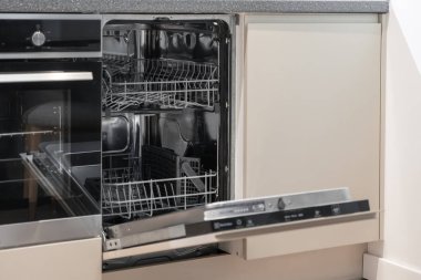 Çağdaş bir mutfak iç mekanına yakın plan, açık bir bulaşık makinesi ve kısmen açık bir fırın, modern yaşamı, işlevselliği ve akıllı ev aletleri çözümlerini sembolize ediyor.