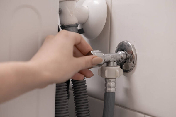 Close-up of a female hand turning a metal valve for water supply control to a household appliance, representing essential home plumbing work and DIY repair