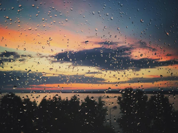 Gota de lluvia en la ventana de vidrio, colorido atardecer, cielo, árboles, lago, amanecer — Foto de Stock