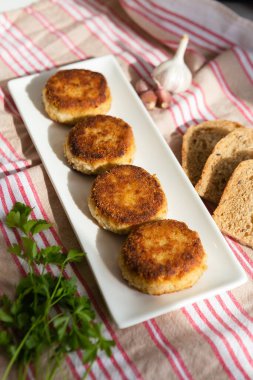 Beyaz dikdörtgen bir tabakta dört adet pirzola var. Beyaz ve kırmızı çizgili havluda ekmek, ot ve sarımsak. Aile için evde öğle yemeği. Yemek pişirmeyle ilgili bir blog için dikey fotoğraf