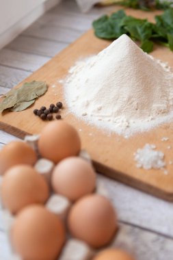 Seçici odaklanma. Vejetaryen yemekleri pişirmek için malzemeler. Un, tavuk yumurtaları, baharatlar ve baharatlar - biber, defne yaprağı, taze ıspanak yaprakları. Parlak bir mutfakta, ahşap bir mutfak tahtasında.