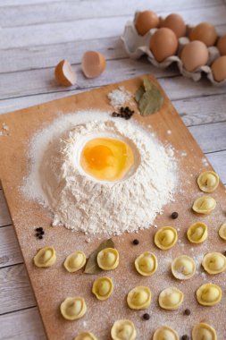 Ev yapımı mantı ve ravioli yaparken yemek masası. Tahtada, un, tavuk yumurtası, defne yaprağı ve bezelye aromalı hazır köfteler var. Yemek pişirme sürecinde nefis ev yemekleri..