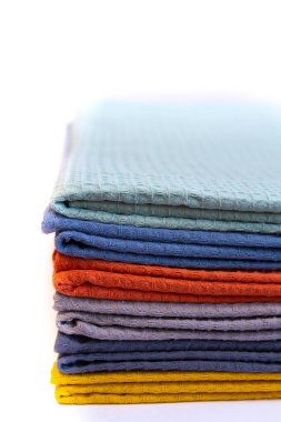 Beyaz arka planda düzgün bir yığın halinde düzenlenmiş renkli mikrofiber havlular. Temizlik, mutfak kullanımı ve ev organizasyonu için çeşitli renklerde parlak ev ürünleri.