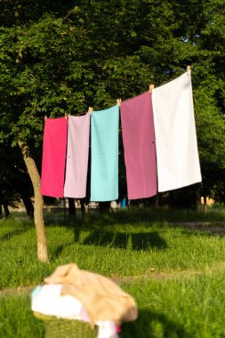 Açık havada çamaşır ipinde asılı renkli tekstil havluları. Taze yıkanmış kumaş doğal güneş ışığında çamaşır mandalları, yumuşak doku, yaz atmosferi, çevre dostu çamaşır konsepti ile kuruyor..
