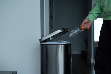 Büyük metal bir çöp kutusuna plastik şişe atmak. Evde çöp ayıklama.