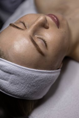 Cilt bakımı sırasında spa yatağında uzanan bir kadının yeni temizlenmiş yüzü pürüzsüz bir ten, sakin bir ifade ve doğal ışık gösteriyor..