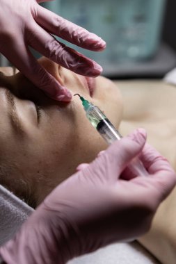 Yüze iğnesiz bir şırıngayla kozmetik uygulamak. Güzellik uzmanının randevusundaki yetişkin hafif kadın. Bir doktorun gözetiminde spa prosedürü