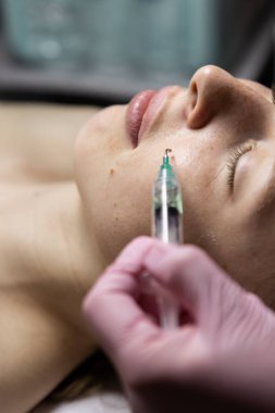Yüze iğnesiz bir şırıngayla kozmetik uygulamak. Güzellik uzmanının randevusundaki yetişkin hafif kadın. Bir doktorun gözetiminde spa prosedürü