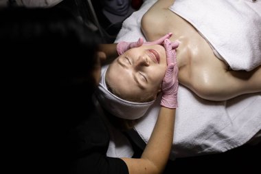 Güzellik uzmanının randevusunda yüz ve boyun masajı. Yetişkin beyaz kadın tedavi görüyor. Pembe lateks eldivenler uzmanı.