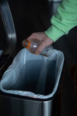 Büyük metal bir çöp kutusuna plastik şişe atmak. Evde çöp ayıklama.