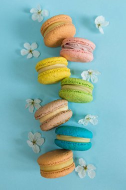 Fransız badem kurabiyeleri, mavi arka planda beyaz çiçekli, narin ışıklandırmalı tatlılar.