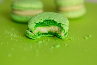 Yeşil arka planda birkaç yeşil badem kurabiyesi var. Biri ısırılmış ve kırıntılar etrafa saçılmış.