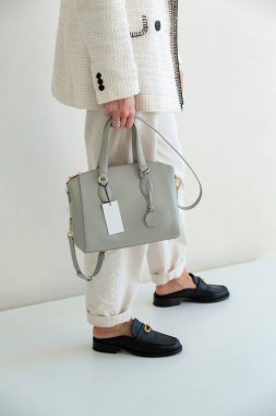 Beyaz takım elbiseli bir kadının açık gri bir el çantası var. Yeni çantasıyla şık bir kız.