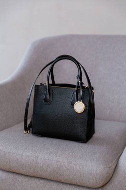 Gri bir sandalyede siyah, küçük bir kadın çantası. Modern moda bir el çantasının fotoğrafı. Günlük yaşamda şık aksesuarlar.