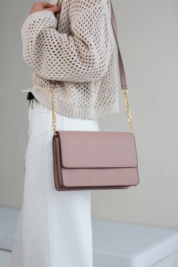 Kız elinde küçük açık pembe kadın çantasıyla pastel arka planda duruyor. Şık aksesuarlar ve giysiler.