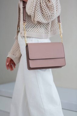 Kız elinde küçük açık pembe kadın çantasıyla pastel arka planda duruyor. Şık aksesuarlar ve giysiler.
