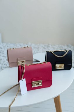 Masada üç el çantası var. Kül pembesi, sıcak pembe ve siyah kadın çantaları açık minimalizmin içinde sergilenmektedir.