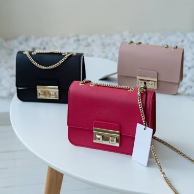 Masada üç el çantası var. Kül pembesi, sıcak pembe ve siyah kadın çantaları açık minimalizmin içinde sergilenmektedir.