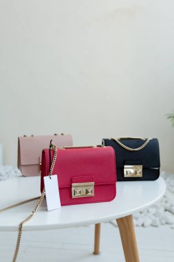 Masada üç el çantası var. Kül pembesi, sıcak pembe ve siyah kadın çantaları açık minimalizmin içinde sergilenmektedir.