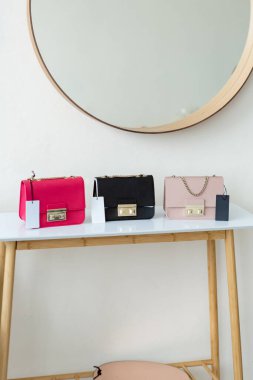 Masada üç el çantası var. Kül pembesi, sıcak pembe ve siyah kadın çantaları açık minimalizmin içinde sergilenmektedir.