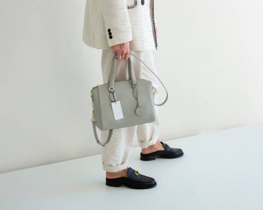 Beyaz takım elbiseli bir kadının açık gri bir el çantası var. Yeni çantasıyla şık bir kız.