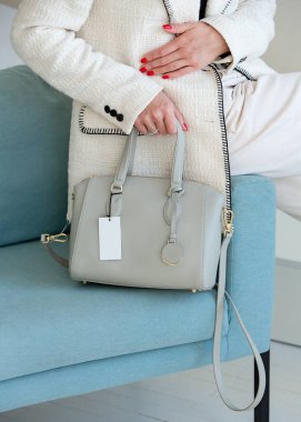 Beyaz takım elbiseli bir kadının açık gri bir el çantası var. Yeni çantasıyla şık bir kız.