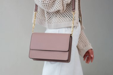 Kız elinde küçük açık pembe kadın çantasıyla pastel arka planda duruyor. Şık aksesuarlar ve giysiler.