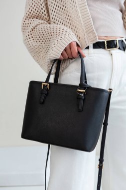 Bir mankenin elinde siyah, küçük bir kadın çantası. Modern moda bir el çantasının fotoğrafı. Günlük yaşamda şık aksesuarlar.