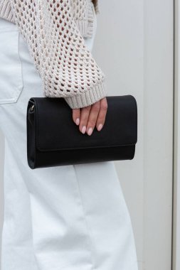 Siyah deri kros çantası, hafif elbiseli bir kadın tarafından tutulan minimalist tasarım.