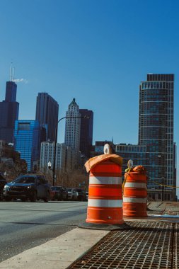 Chicago şehir merkezindeki işlek bir caddede trafik turuncu inşaat bariyerlerini aşıyor. Bölgedeki çalışmalar devam ederken yüksek binalar mavi gökyüzüne doğru uzanıyor.