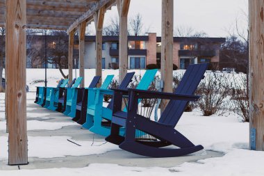 Mavi ve yeşil renkli sallanan sandalyeler ahşap bir yapının altında düzenlenir. Etraflarındaki zemini kar kaplıyor ve arka planda yakınlardaki binalar görülebiliyor..