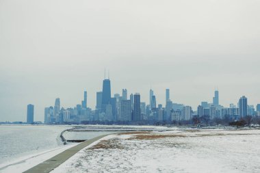 Michigan Gölü kıyısı boyunca kar zemini kaplıyor. Chicago silueti kış boyunca gri gökyüzüne karşı yüksek binalar gösteriyor. Manzara soğuk havada kentsel manzarayı yakalar..