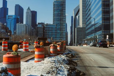 İşçiler, modern binalar ve trafik konileriyle çevrili bir şehir caddesinde öğleden sonra saatlerinde açık mavi bir gökyüzünün altında inşaat yapıyorlar..