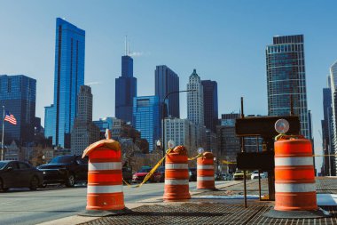 Şikago şehir merkezinde bir şehir caddesinde inşaat bariyerleri kuruldu. Arabalar geçiyor ve arka planda açık bir gökyüzünün altında yüksek binalar görülüyor..