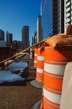 İnşaat işçileri sokağa güvenlik bariyerleri koydular. Şehir binaları parlak mavi gökyüzünün altında arka planda yükseliyor. Kar yerde kalır..