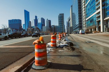 İşçiler Chicago şehir merkezindeki bir caddede inşaat konileri bölgeyi işaretlerken görüldüler. Arka planda uzun binalar var ve gökyüzü temiz..