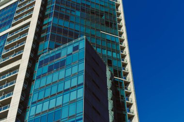 Yüksek ofis binası parlak cam bir cephe ile ayakta duruyor. Yapının mavi gökyüzünü yansıtan birçok penceresi vardır. Binanın dış tarafında parlak güneş ışığı parlıyor..