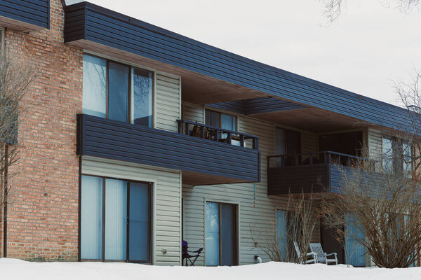 The structure shows a contemporary design with large windows and balconies. Snow covers the ground, highlighting the winter season in the neighborhood.
