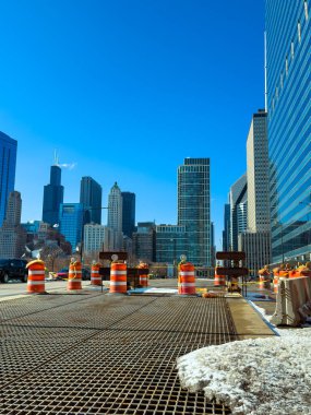 İşçiler Chicago 'da işlek bir caddeye inşaat bariyerleri kuruyorlar. İlkbaharda açık mavi bir gökyüzünün altındaki yüksek binalar bölgeyi çevreledi..
