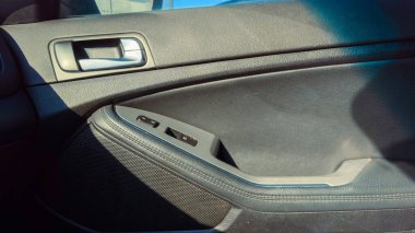 Yakın görüntü arabanın kapı panelini ve pencere kontrollerini gösteriyor. Araba park halindeyken, içerisi güneş ışığıyla aydınlık..