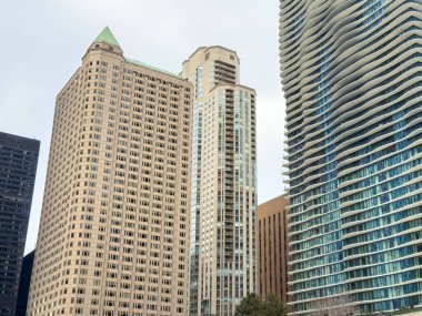 Şehir merkezindeki kalabalık binalar modern ve geleneksel tarzların bir karışımını gösteriyor. Gökyüzü bulutlu ve insanlar yakınlarda yürürken görülebilir..