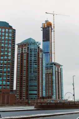 İşçiler suya yakın yüksek bir bina inşaatına devam ederken, diğer binalar da kış günü çevreyi sarıyorlar..