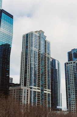 Yüksek binalar gün boyunca bulutlu bir gökyüzü olan şehir ortamında dururlar. Sahne modern mimariyi gösteriyor..