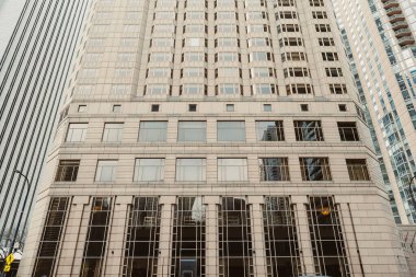 Gün boyunca açık gökyüzü olan kentsel bir alanda uzun binalar cadde boyunca sıralanır. Pencereler ışığı ön cephelere yansıtır.