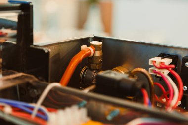 Mekanik bileşenler turuncu tüpler, metal montajlar ve gündüz saatlerinde bir atölyede birden fazla kablo bulunan bir makinenin içinde görülebilir..