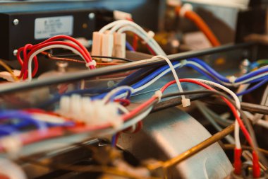 Atölyedeki bir makinedeki kablolara ve bağlantılara odaklan. Çeşitli renkli kablolar farklı parçaları birbirine bağlar, elektrik sistemlerinin karmaşıklığını gösterir.