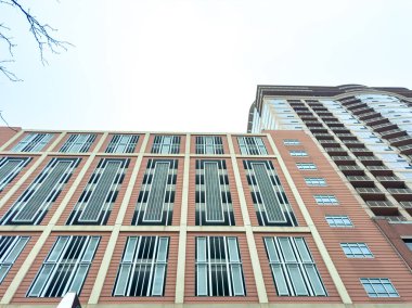 People can see several tall buildings rising into the sky with a gray background. The structures have many windows and different colors. This scene shows city life.